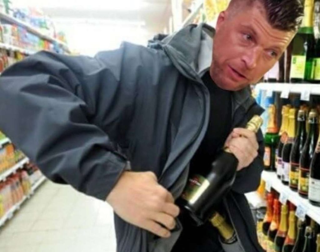 Man tucking a bottle into his jacket in a store aisle